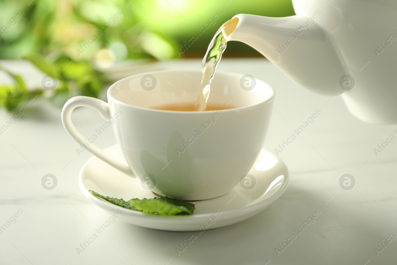 Pouring freshly brewed tea from teapot into cup at white marble table, closeup Photo of Pouring freshly brewed tea from teapot into cup at white marble table, closeup
