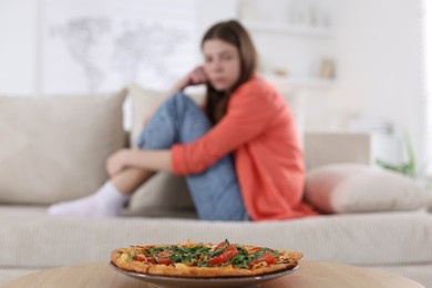 Photo of Sad teen girl looking at pizza indoors, selective focus. Eating disorder