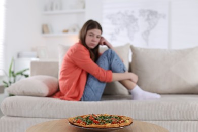 Photo of Sad teen girl looking at pizza indoors, selective focus. Eating disorder