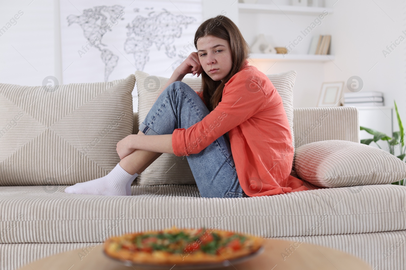 Photo of Sad teen girl looking at pizza indoors. Eating disorder