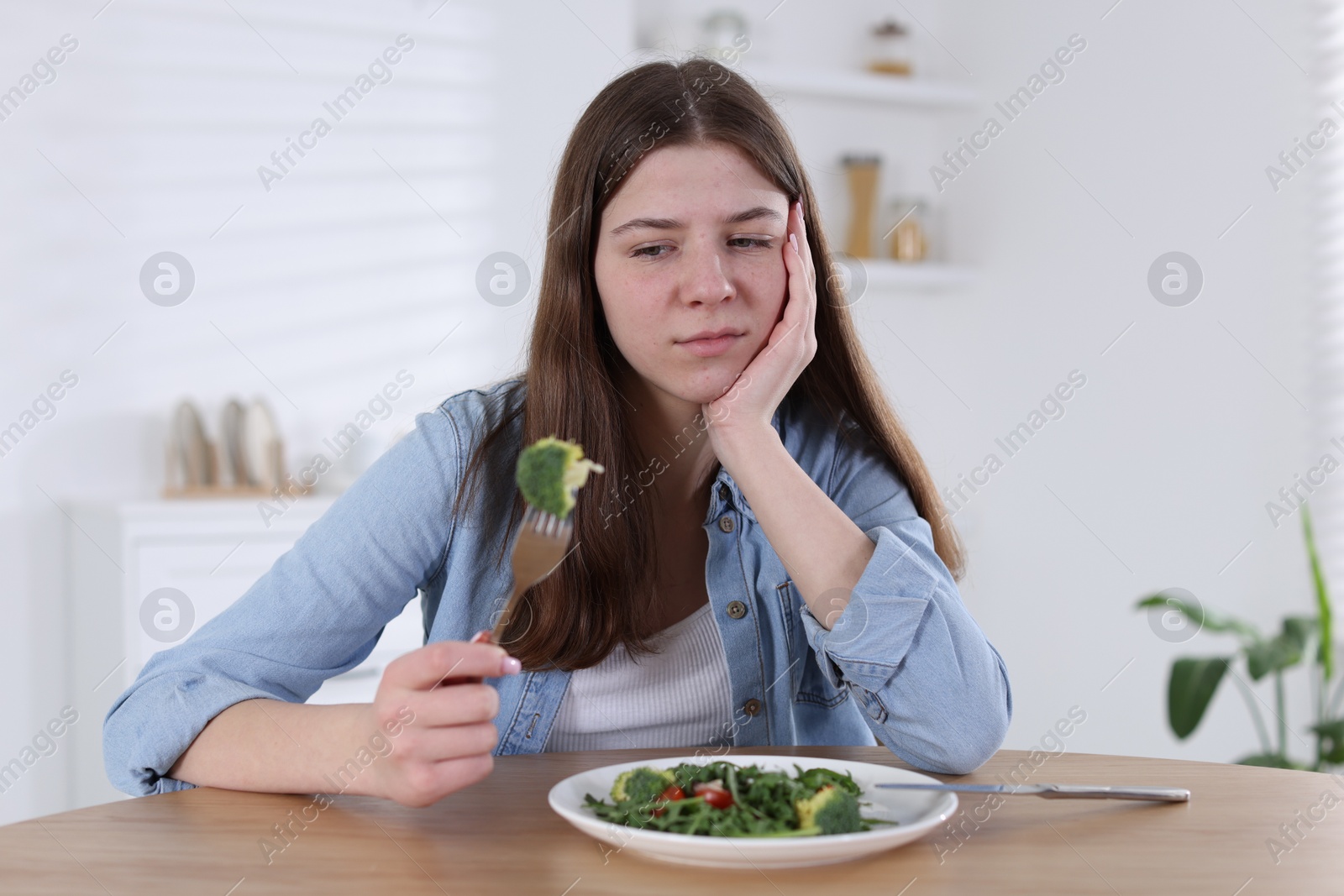 Photo of Sad teen girl holding fork with broccoli at home. Eating disorder