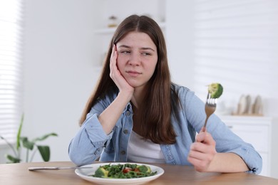 Photo of Sad teen girl holding fork with broccoli at home. Eating disorder