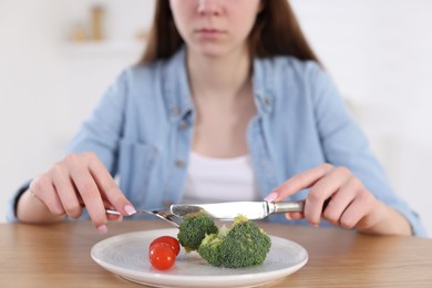 Photo of Sad teen girl cutting broccoli at home, closeup. Eating disorder