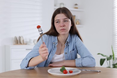 Photo of Sad teen girl holding fork with tomato at home. Eating disorder