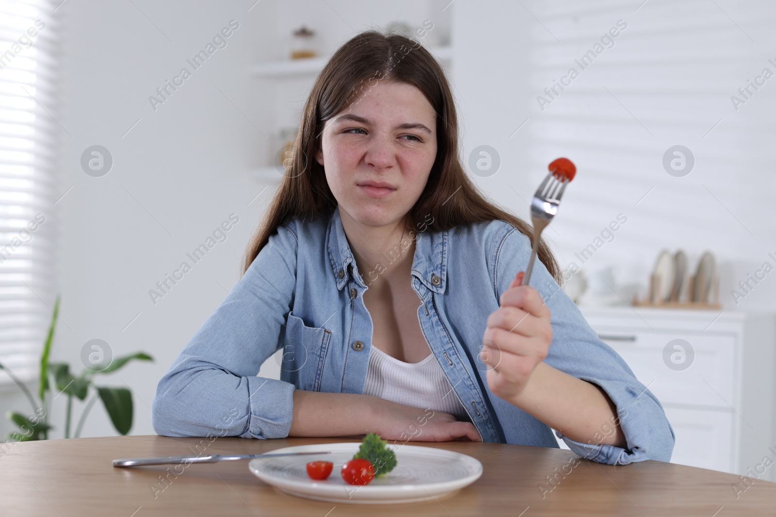 Photo of Sad teen girl holding fork with tomato at home. Eating disorder