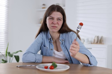 Photo of Sad teen girl holding fork with tomato at home. Eating disorder