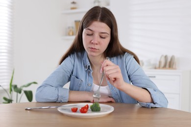 Photo of Sad teen girl holding fork with broccoli at home. Eating disorder