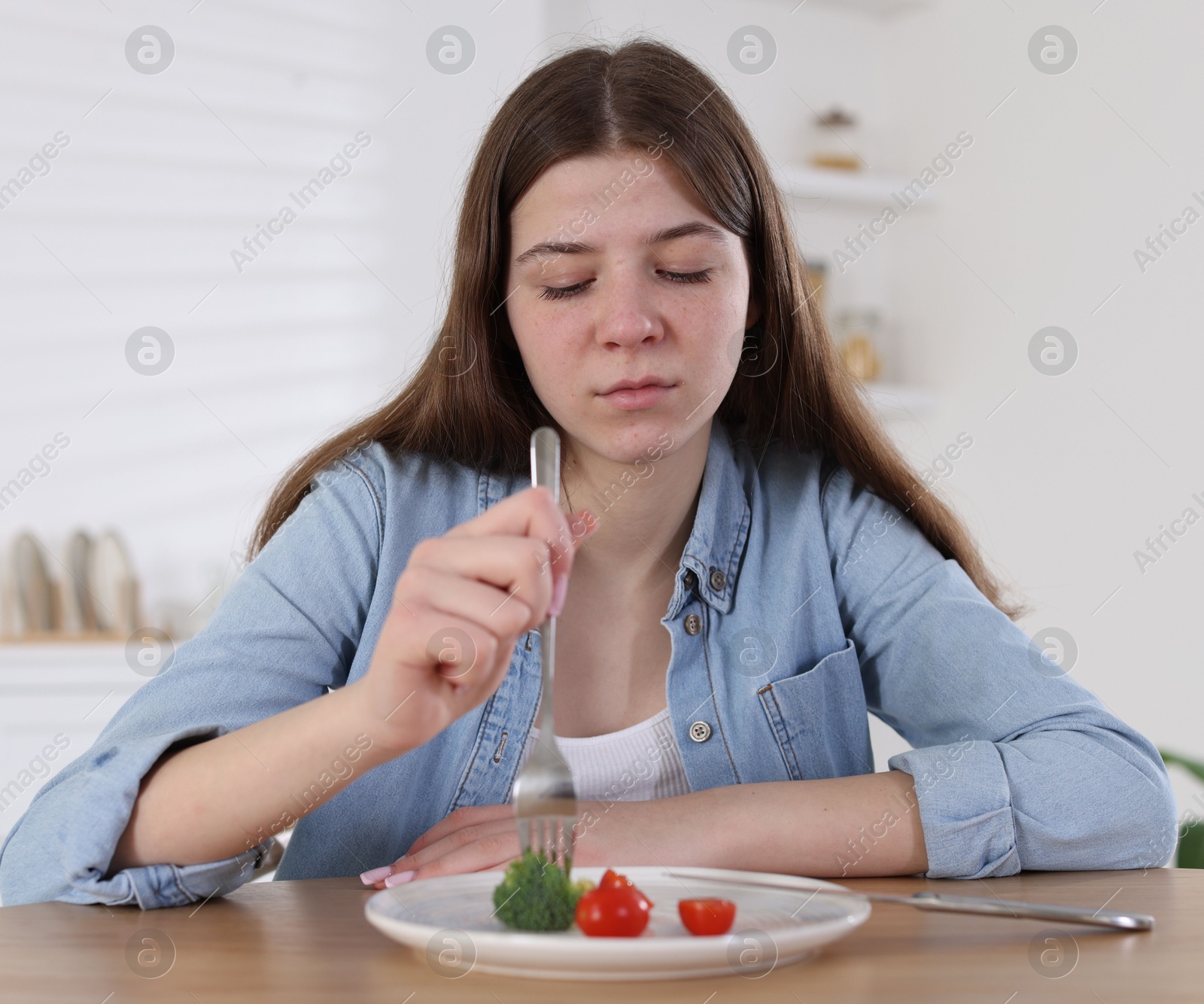 Photo of Sad teen girl holding fork with broccoli at home. Eating disorder