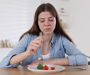 Photo of Sad teen girl holding fork with broccoli at home. Eating disorder