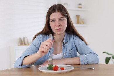 Photo of Sad teen girl holding fork with broccoli at home. Eating disorder