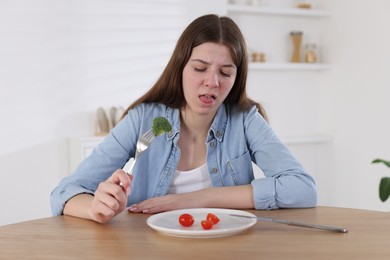 Photo of Sad teen girl holding fork with broccoli at home. Eating disorder