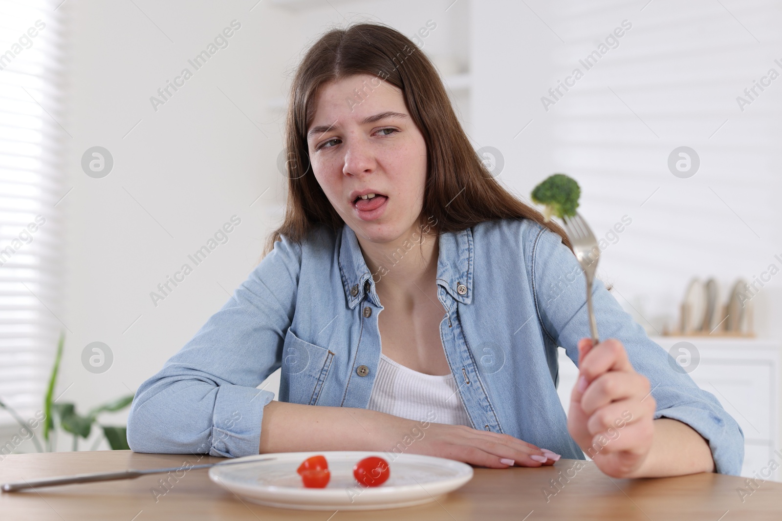 Photo of Sad teen girl holding fork with broccoli at home. Eating disorder