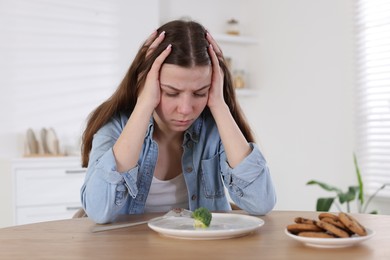 Photo of Sad teen girl at table with broccoli indoors. Eating disorder