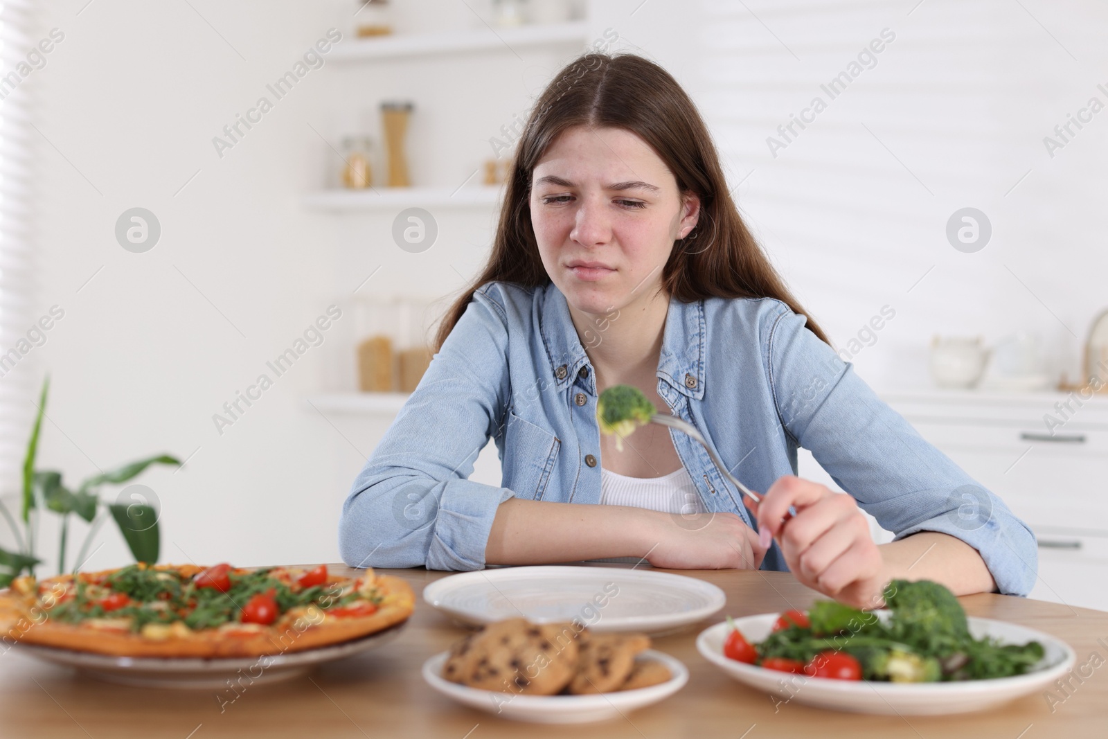 Photo of Sad teen girl holding fork with broccoli at home. Eating disorder