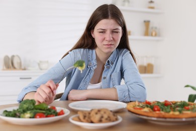 Photo of Sad teen girl holding fork with broccoli at home. Eating disorder