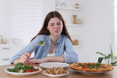 Photo of Sad teen girl holding fork with broccoli at home. Eating disorder