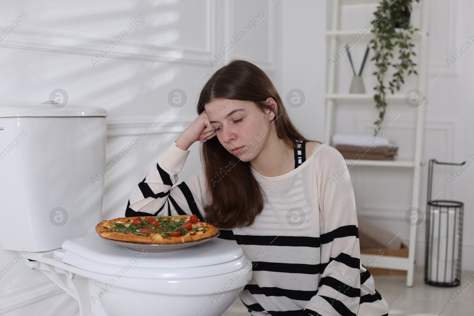 Photo of Teen girl with pizza near toilet bowl at home. Bulimia