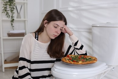 Photo of Teen girl with pizza near toilet bowl at home. Bulimia