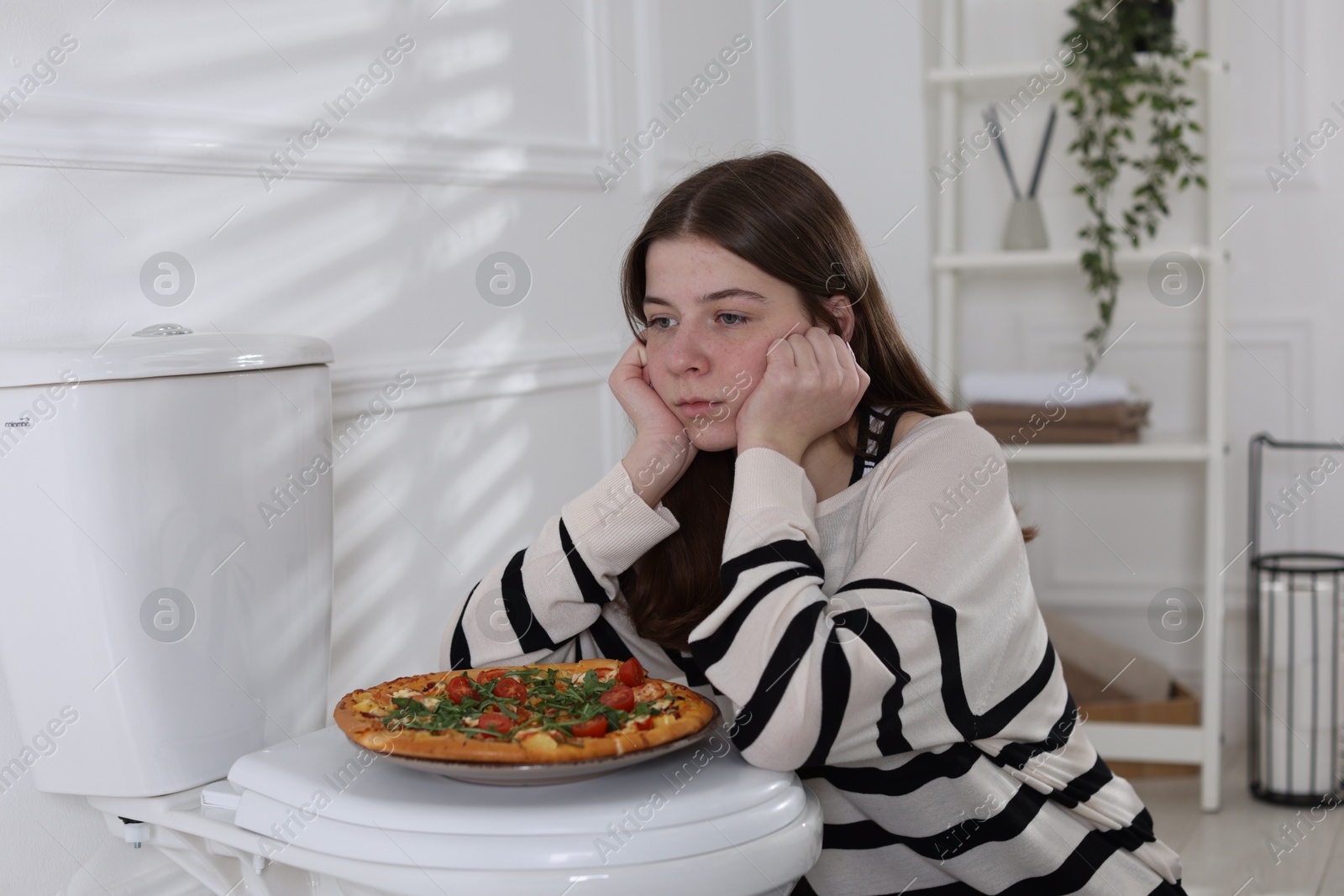 Photo of Teen girl with pizza near toilet bowl at home. Bulimia