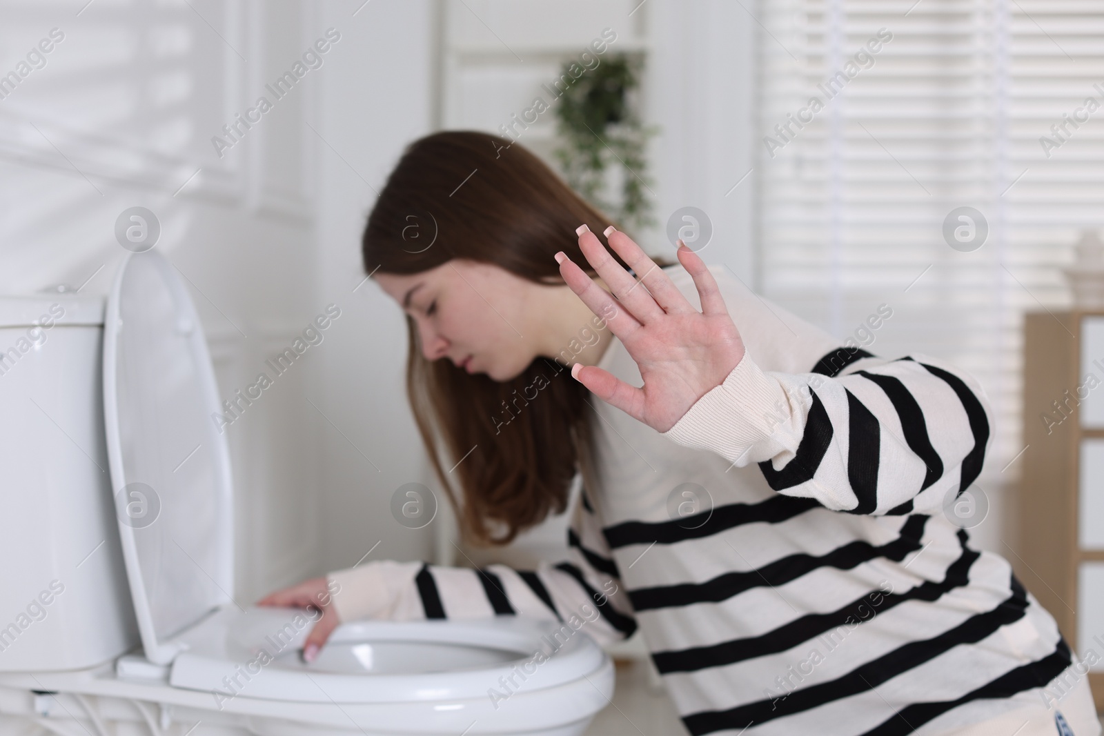 Photo of Teenage girl suffering from nausea over toilet bowl showing stop gesture indoors, selective focus. Bulimia