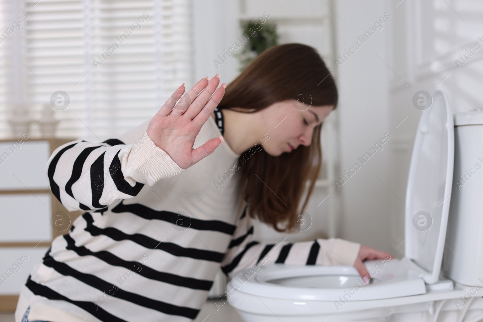 Photo of Teenage girl suffering from nausea over toilet bowl showing stop gesture indoors, selective focus. Bulimia