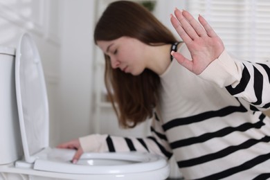 Photo of Teenage girl suffering from nausea over toilet bowl showing stop gesture indoors, selective focus. Bulimia