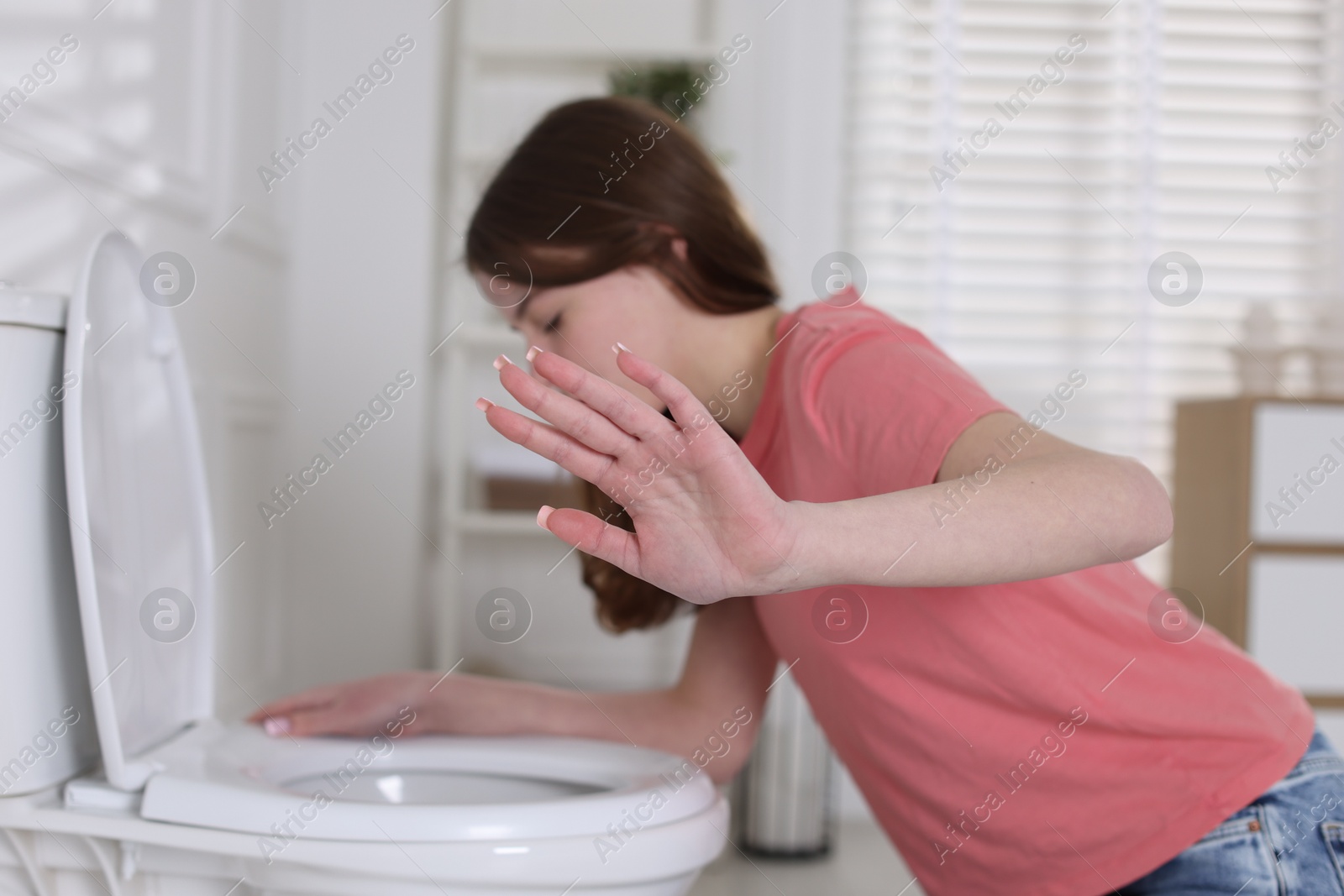 Photo of Teenage girl suffering from nausea over toilet bowl showing stop gesture indoors, selective focus. Bulimia