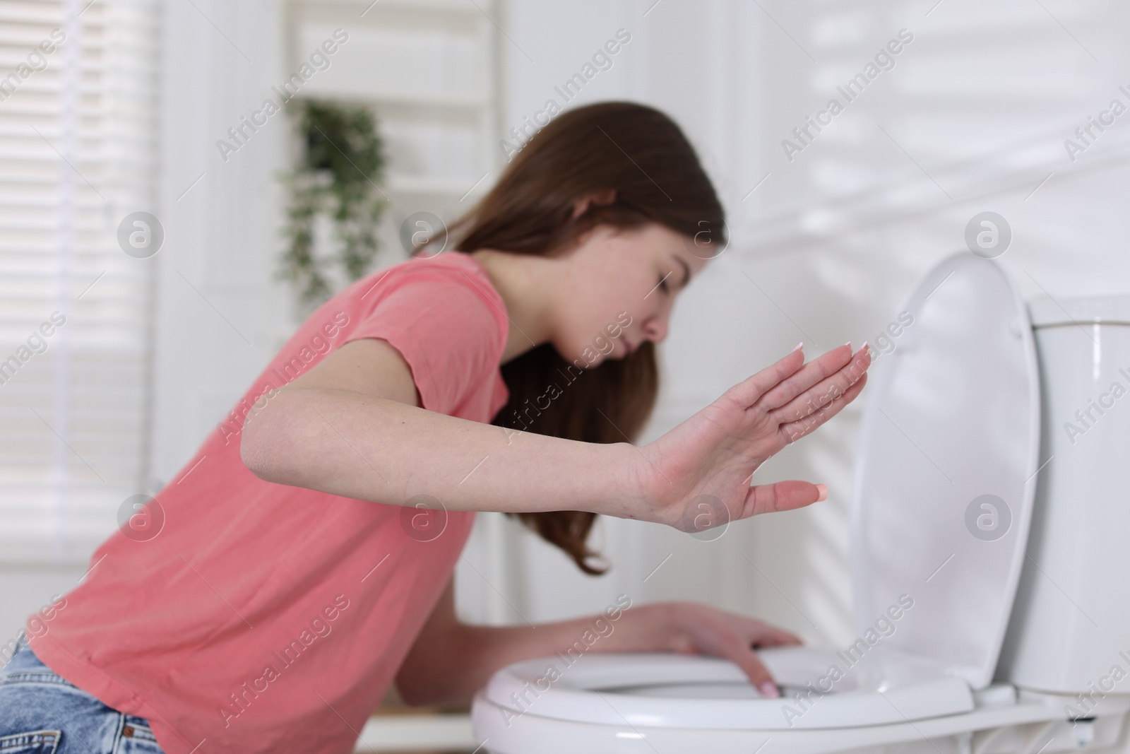 Photo of Teenage girl suffering from nausea over toilet bowl showing stop gesture indoors, selective focus. Bulimia