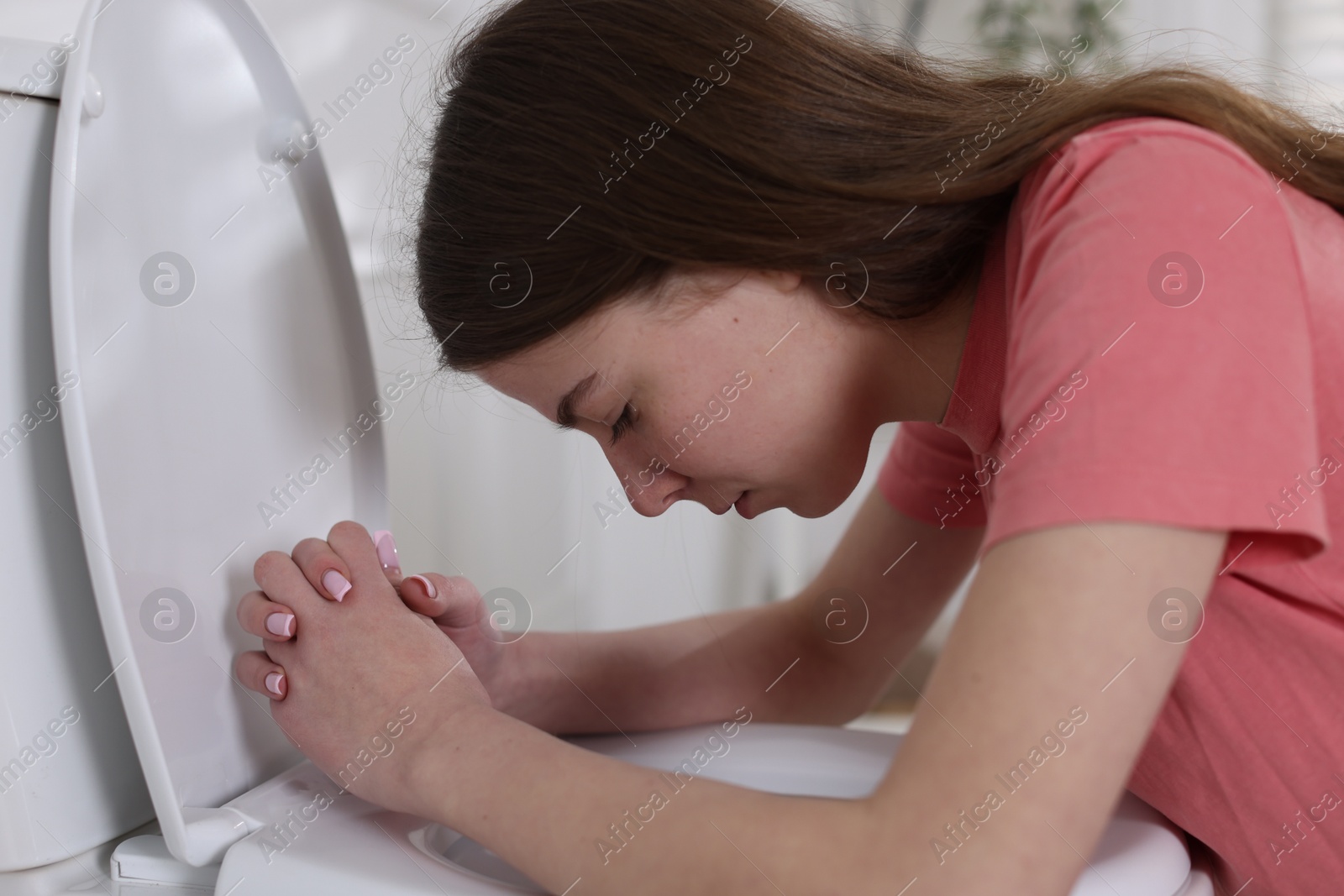 Photo of Teenage girl suffering from nausea over toilet bowl indoors. Bulimia