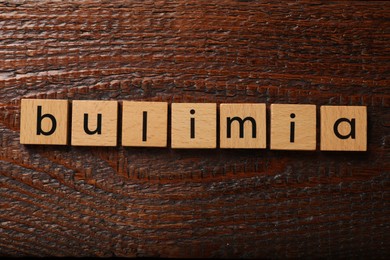 Photo of Squares with word Bulimia on wooden table, flat lay