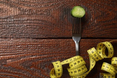 Photo of Bulimia. Fork with slice of cucumber and measuring tape on wooden table, flat lay. Space for text