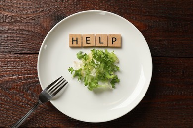 Photo of Bulimia. Squares with word Help, plate, salad and fork on wooden table, top view