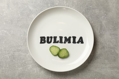 Photo of Plate with word Bulimia and cut cucumber on grey table, top view