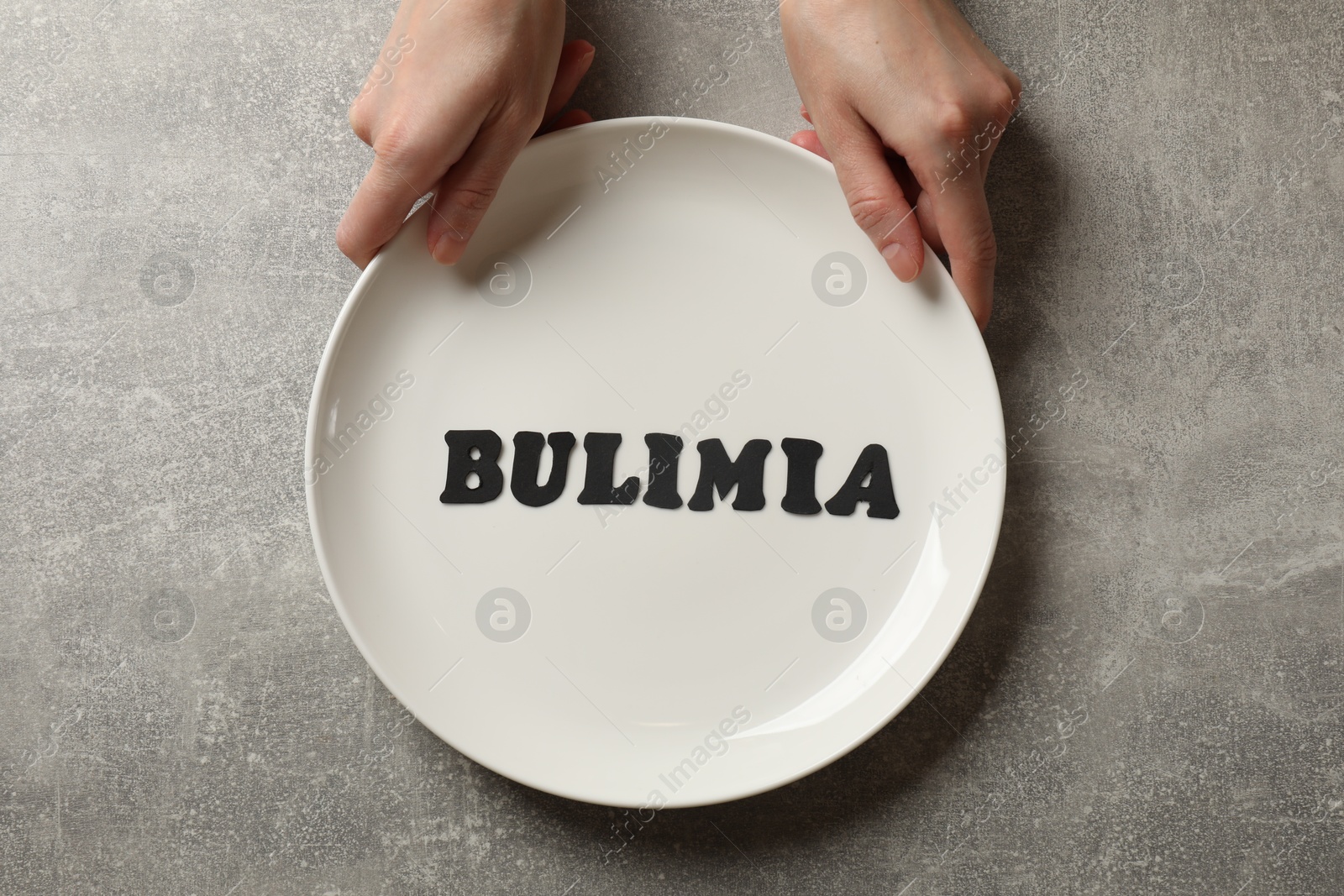 Photo of Bulimia. Woman with plate at grey table, top view