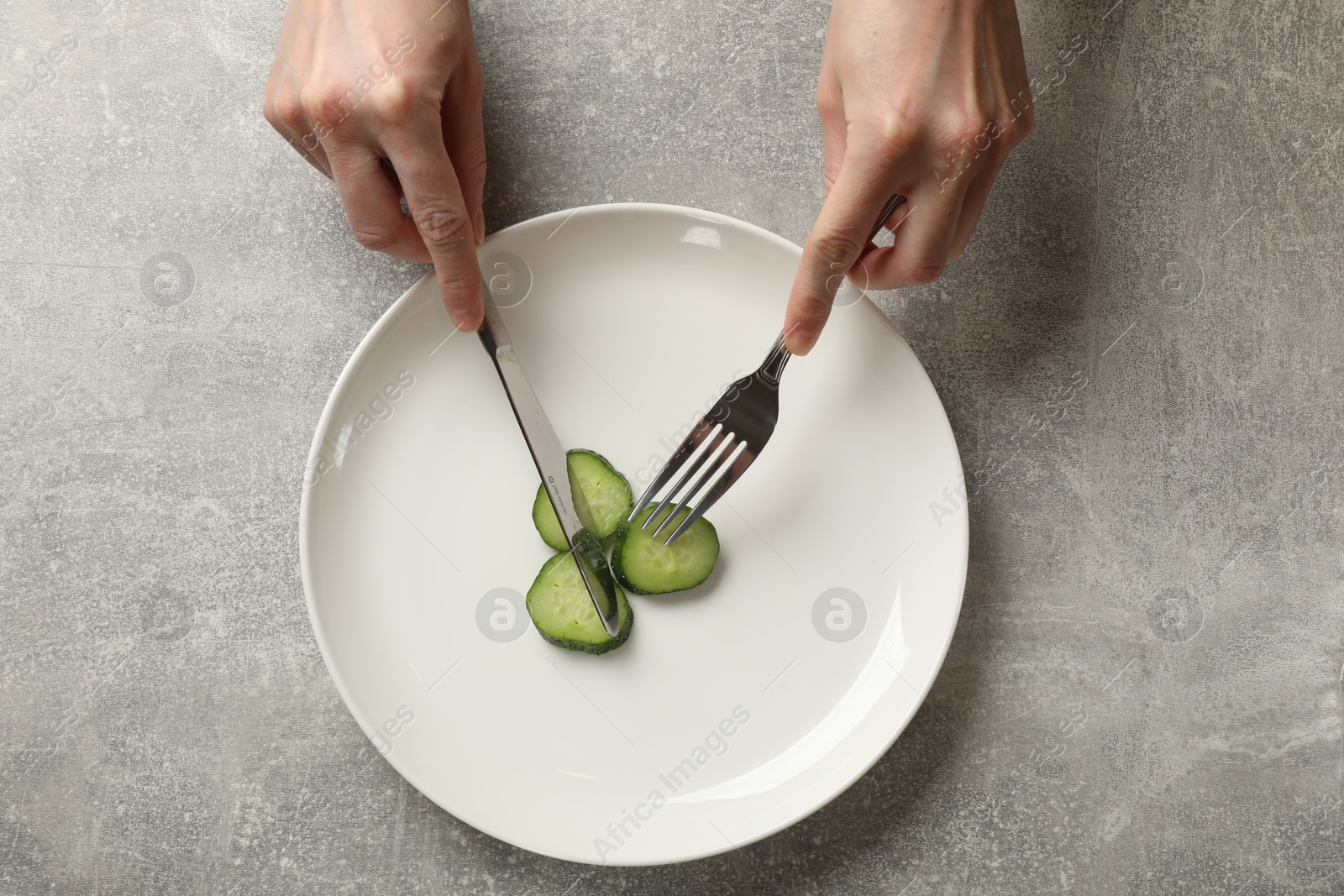 Photo of Bulimia. Woman cutting cucumber at grey table, top view