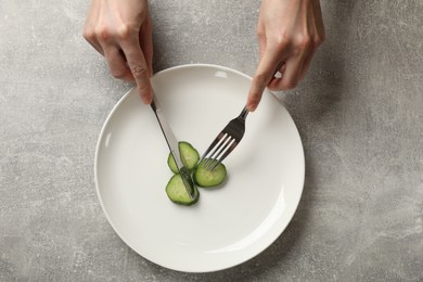 Photo of Bulimia. Woman cutting cucumber at grey table, top view