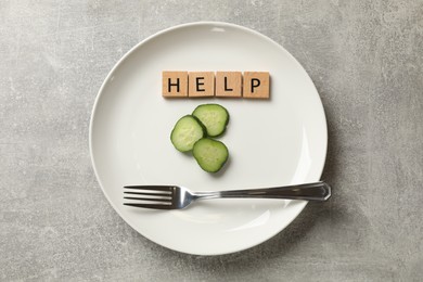 Photo of Bulimia. Squares with word Help, plate, cut cucumber and fork on grey table, top view