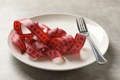 Photo of Bulimia. Fork, plate and measuring tape on grey table, closeup