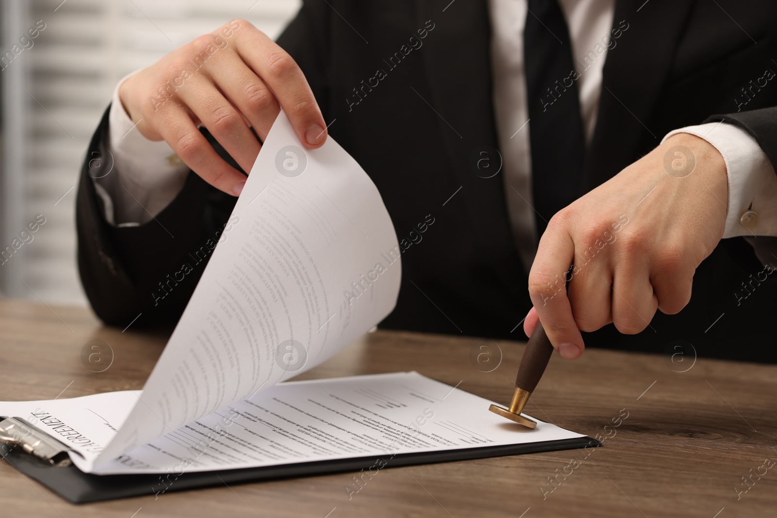 Photo of Man stamping licensing agreement document at wooden table indoors, closeup