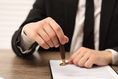 Photo of Man stamping licensing agreement document at wooden table indoors, closeup