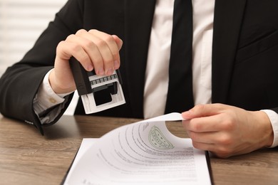 Photo of Man stamping licensing agreement document at wooden table indoors, closeup