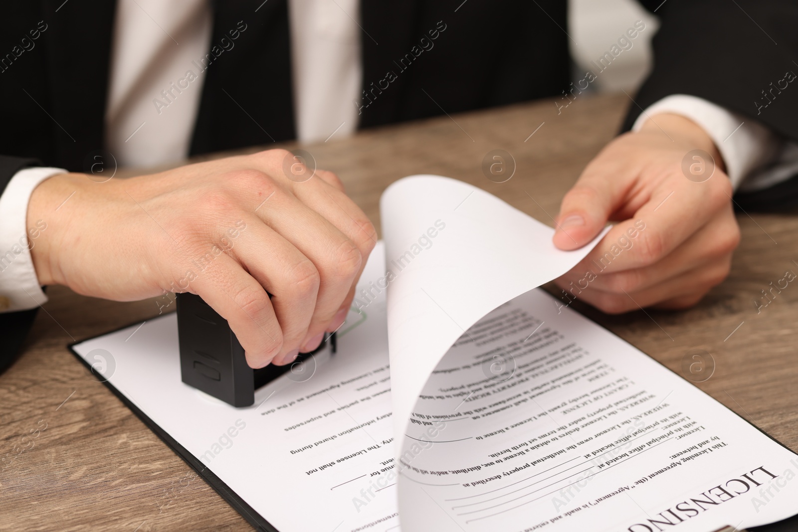 Photo of Man stamping licensing agreement document at wooden table indoors, closeup