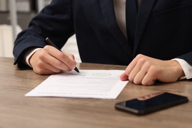 Photo of Man signing licensing agreement document at wooden table indoors, closeup