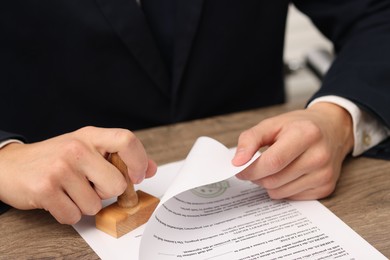 Photo of Man stamping licensing agreement document at wooden table indoors, closeup