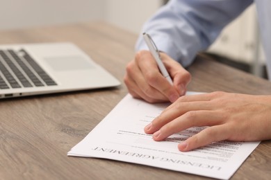 Photo of Man signing licensing agreement document at wooden table indoors, closeup