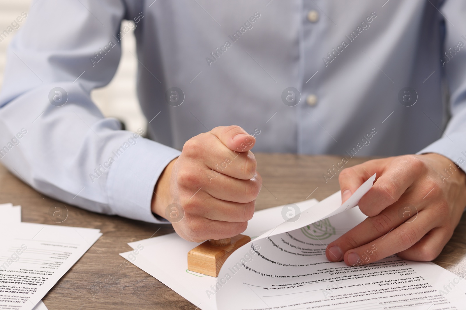 Photo of Man stamping licensing agreement document at wooden table indoors, closeup