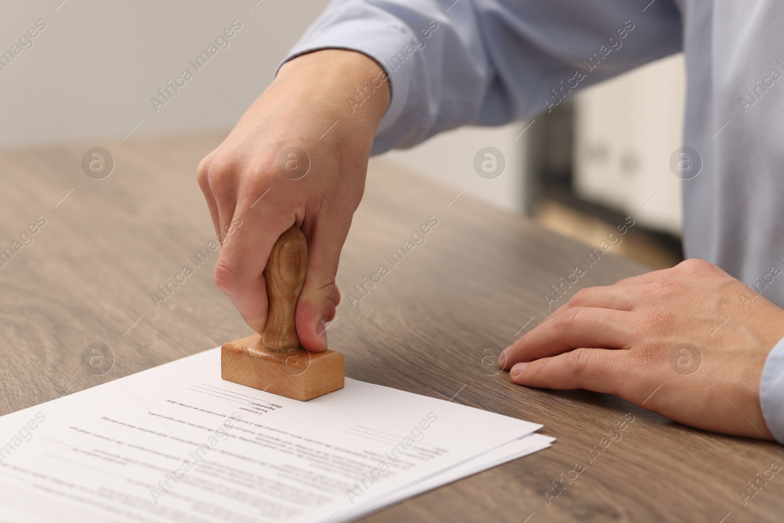 Photo of Man stamping licensing agreement document at wooden table indoors, closeup