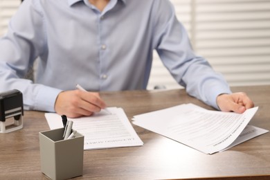 Photo of Man signing licensing agreement document at wooden table indoors, closeup