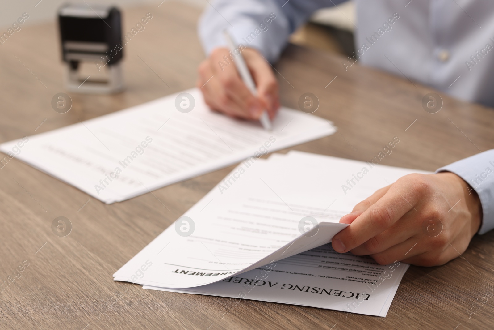 Photo of Man signing licensing agreement document at wooden table indoors, closeup