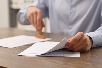 Photo of Man stamping licensing agreement document at wooden table indoors, closeup